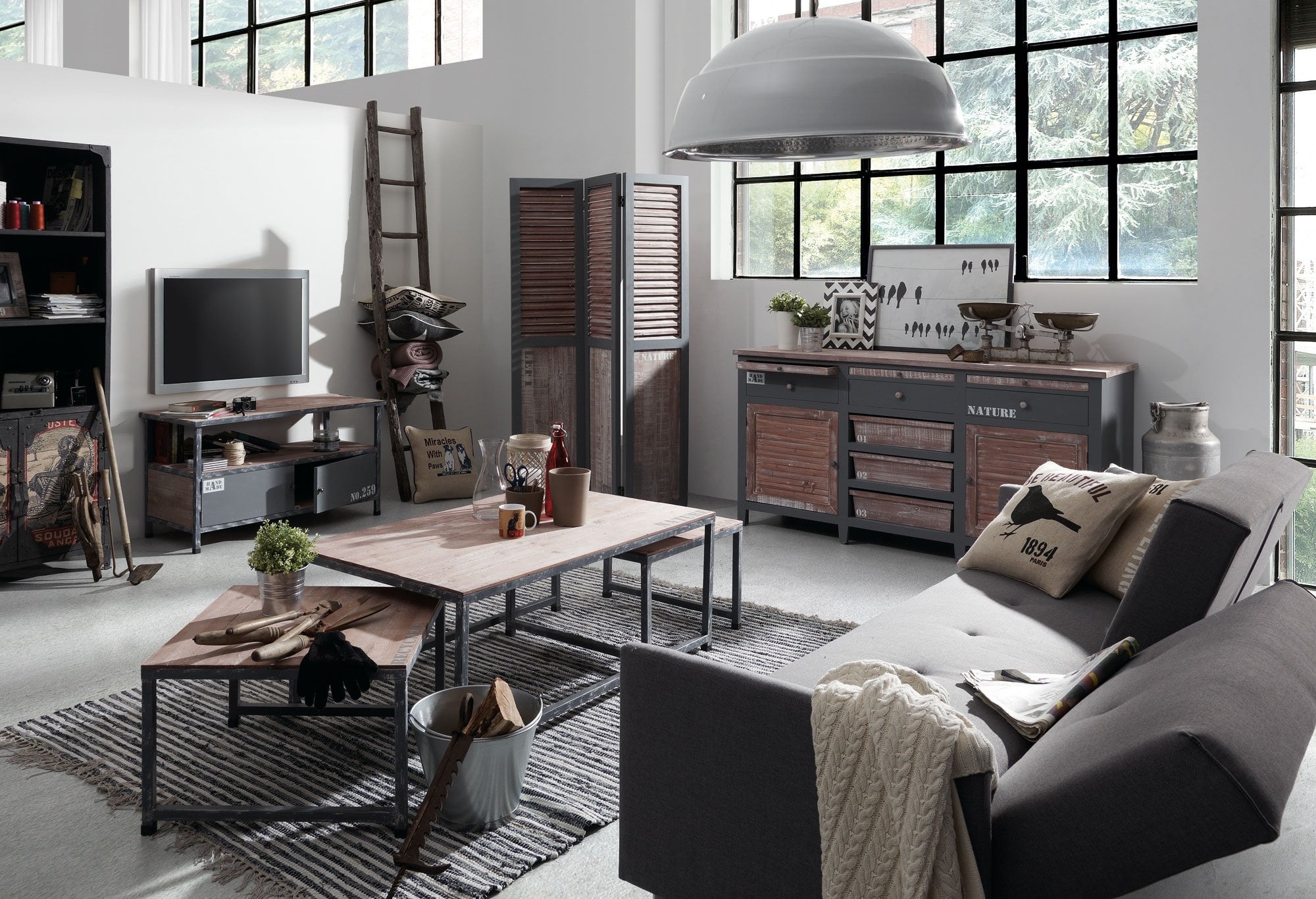 Salón con muebles de estilo industrial, sofá gris, mesas de madera y metal, y aparador rústico en un espacio luminoso.
