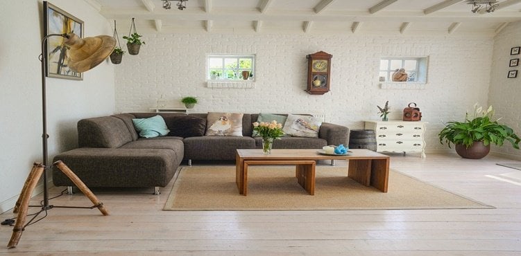 Salón rústico moderno con sofá marrón, vigas de madera expuestas y paredes de ladrillo blanco con decoración acogedora.
