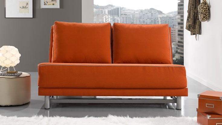 Sofá cama naranja de dos plazas con diseño moderno, cojines grandes y estructura metálica en un salón contemporáneo.
