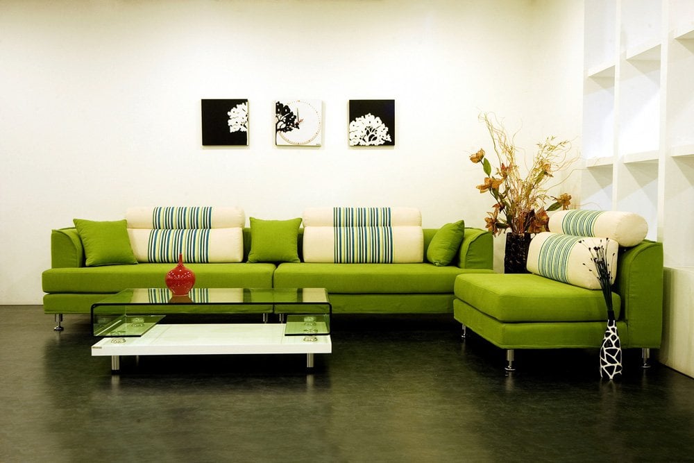 Sofá modular verde lima con cojines de rayas azules y blancas, mesa de centro de cristal y cuadros modernos en la pared