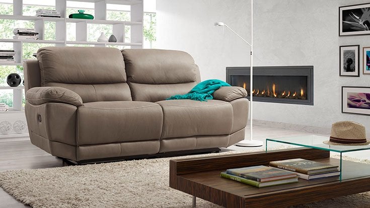 Sofá reclinable de cuero taupe en un salón moderno con chimenea encendida y mesa de centro con libros